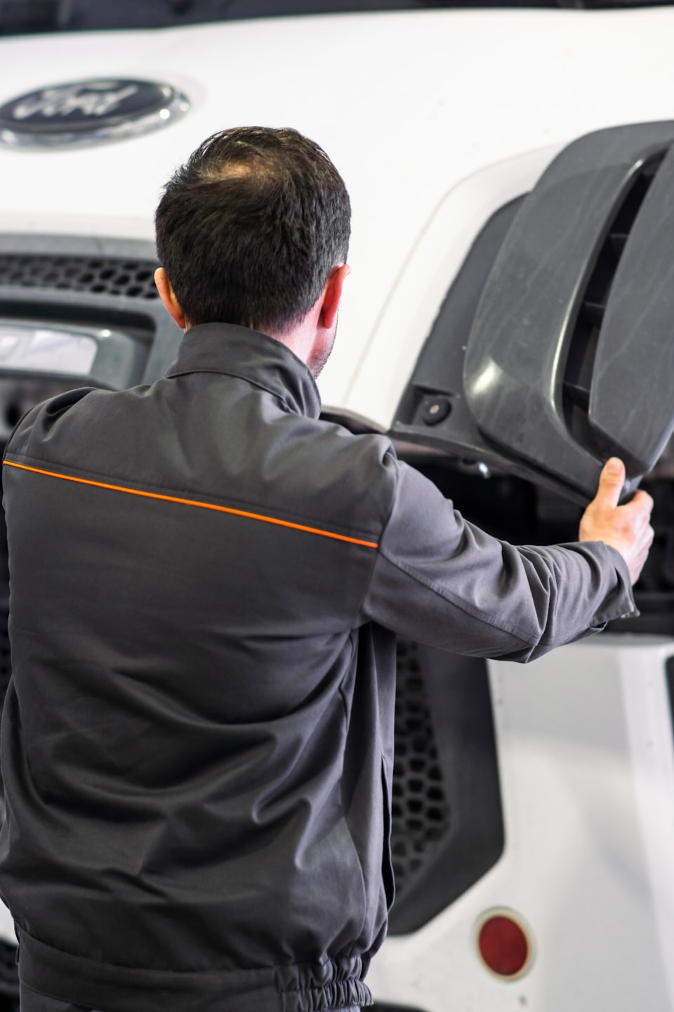 Mechaniker inspiziert großen Fahrzeugmotorraum und hält eine graue Platte.